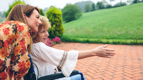 smiling woman in wheelchair with daughter looking out into green garden